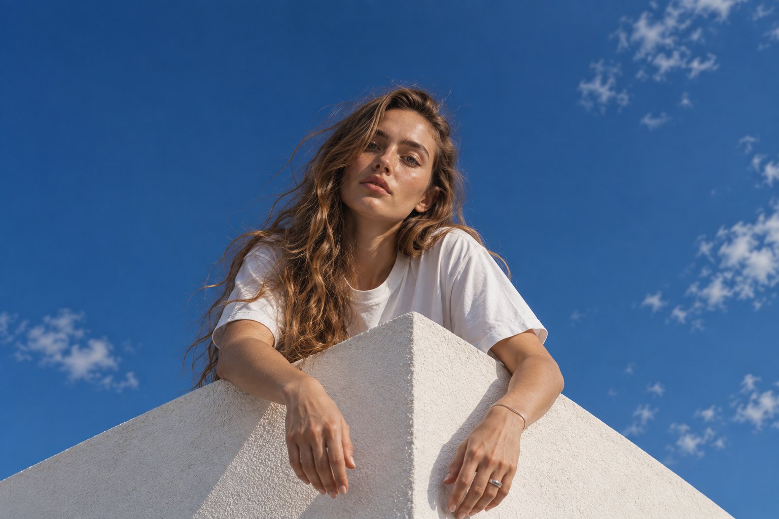 A woman leaning over a white wall under a blue sky